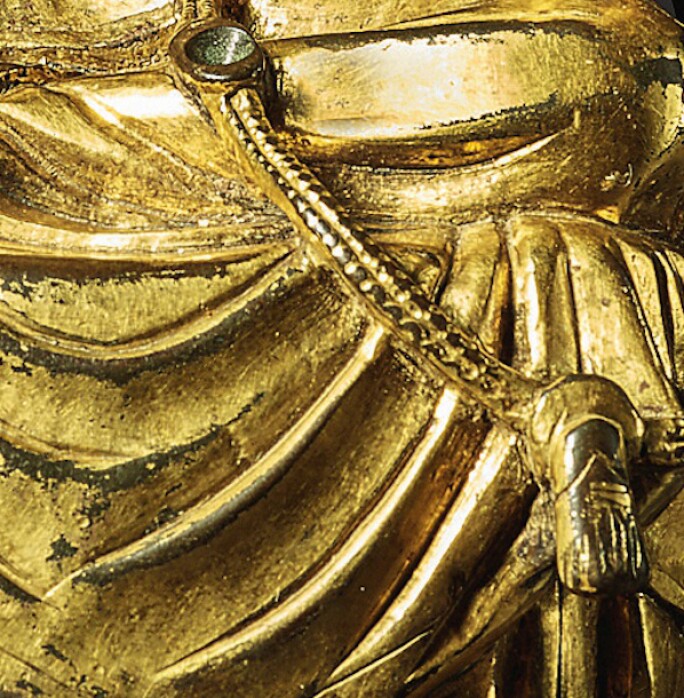 Detail of golden statue depicting a buddha, focused on the area resembling flowing drapery