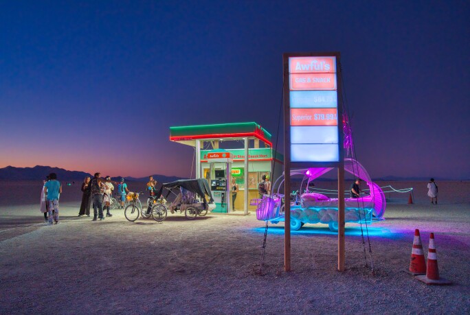 Petrol station in the desert surrounded by people, a bicycle, a neon sign, traffic cones and other objects