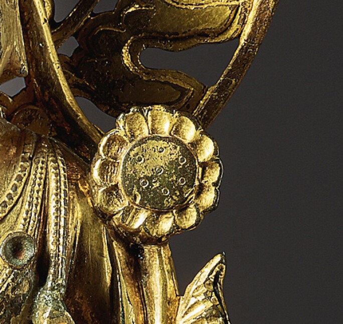 Detail of a golden statue depicting a buddha, focused on the area resembling a floral jewel