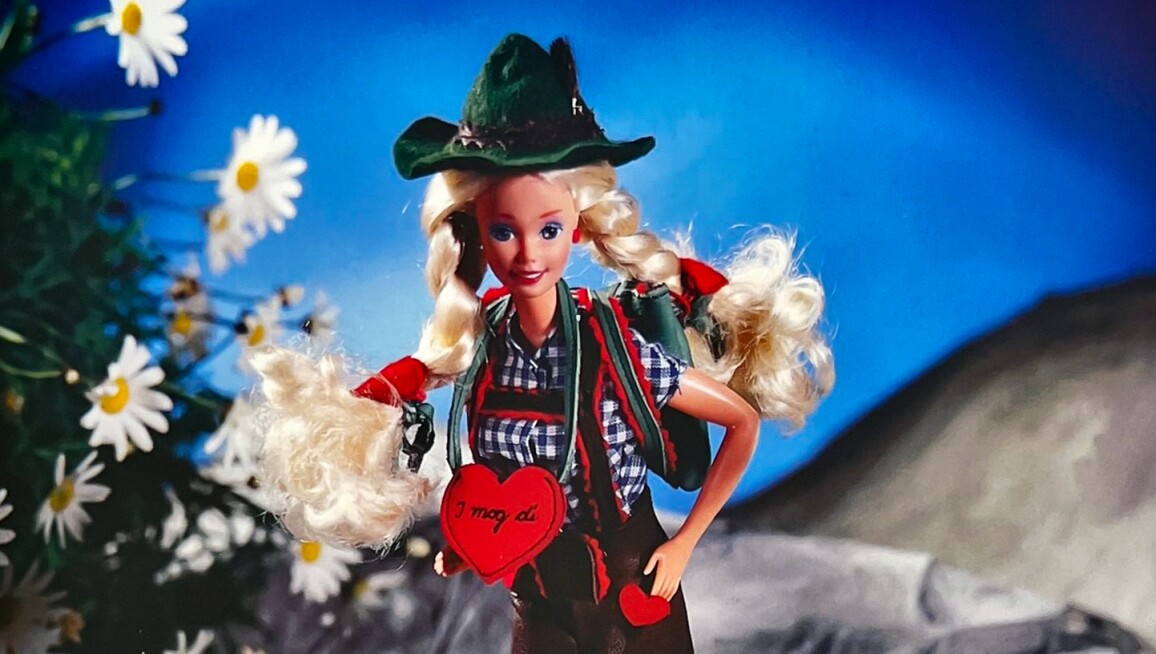 Barbie is going to the mountains with leather trousers and a plaid shirt. She has woolen stockings, mountain boots and a Tyrolean hat. in her green backpack she finds a pretzel, white sausages and a hearty pint of beer.