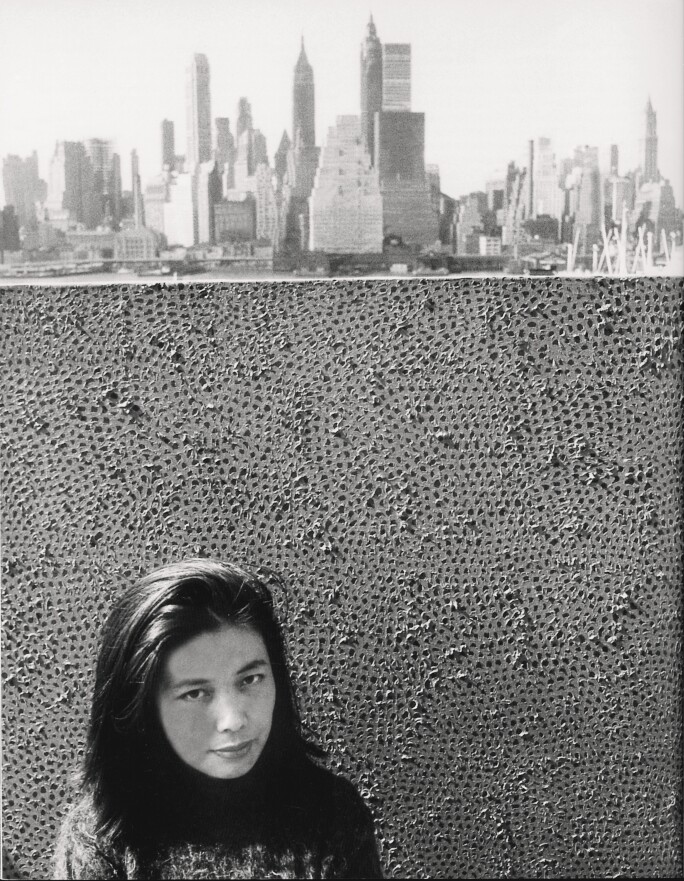 Yayoi Kusama standing with her work against a background of Manhattan, NY in 1961. Courtesy YAYOI KUSAMA Inc.