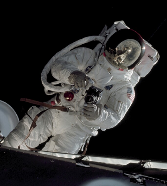 Astronaut Russell L. Schweickart, lunar module pilot, operates a 70mm Hasselblad camera during his extravehicular activity on the fourth day of the Apollo 9 earth-orbital mission. The Command/Service Module and the Lunar Module 3 "Spider" are docked. This view was taken form the Command Module "Gumdrop". Schweickart, wearing an Extravehicular Mobility Unit (EMU), is standing in "golden slippers" on the Lunar Module porch. On his back, partially visible, are a Portable Life Support System (PLSS) and an Oxygen Purge System (OPS). Film magazine was A,film type was SO-368 Ektachrome with 0.460 - 0.710 micrometers film / filter transmittance response and haze filter,80mm lens.