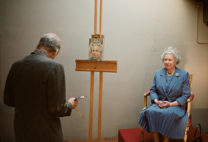 A photograph of Her Majesty Queen Elizabeth II in a slate gray suit, having her portrait painted.